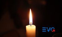 Weiße brennende Kerze vor dunklem, unscharfem Hintergrund; rechts unten ist ein blau-rotes „EVG“-Logo sichtbar.