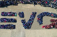 Menschen formen aus der Vogelperspektive die Buchstaben „EVG“ auf einem gepflasterten Platz.