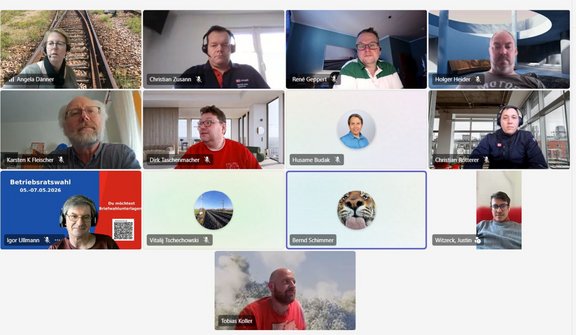 Screenshot einer Videokonferenz mit einer rasterförmigen Anordnung mehrerer Kacheln. In den Kacheln sind überwiegend Oberkörper vor unterschiedlichen Hintergründen zu sehen, darunter Innenräume, Fenster, Arbeitsräume, eine Bahnstrecke im Freien sowie Profilbilder mit Landschafts- oder Tiermotiv. In mehreren Kacheln sind Namensbeschriftungen eingeblendet, darunter „Angela Danner“, „Christian Zusann“, „René Geppert“, „Holger Heider“, „Karsten K. Fleischer“, „Dirk Taschenmacher“, „Husam Budak“, „Christian Retterer“, „Igor Ullmann“, „Vitalij Tschechowski“, „Bernal Schimmer“, „Witecek, Justin“ und „Tobias Koller“. Eine Kachel zeigt ein rotes Plakat mit der Aufschrift „Betriebsratswahl 05.–07.05.2026“ sowie einem QR-Code. Eine Kachel ist mit einem blauen Rahmen hervorgehoben.