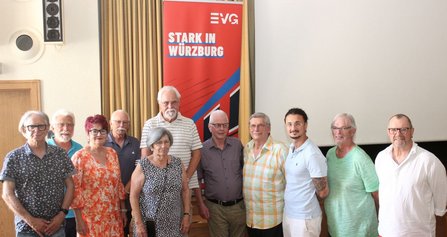 Eine Gruppe von Menschen steht nebeneinander in einem Raum vor einem roten Banner mit der Aufschrift „STARK IN WÜRZBURG“. Die Personen tragen unterschiedliche Kleidung und blicken in die Kamera.
