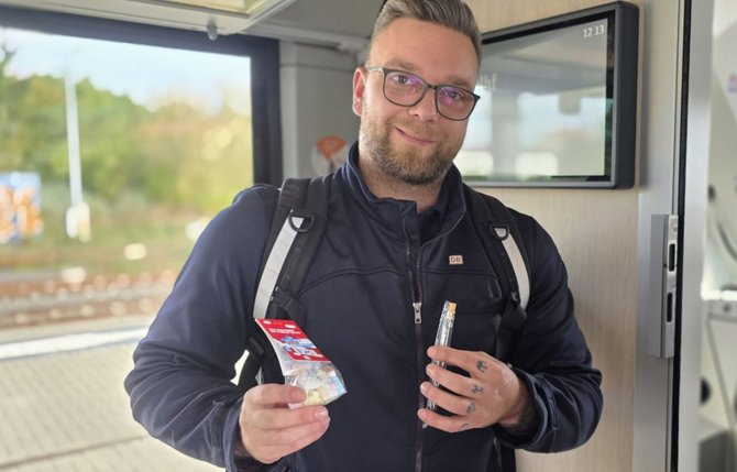 Zwei Personen stehen auf einem Bahnsteig vor einem Triebzug. Beide halten kleine rote beziehungsweise helle Gegenstände in den Händen. Die Person rechts steht neben einem roten Rollkoffer mit der Aufschrift „EVG-TARIFKOFFER“. Am Zug sind technische Kennzeichnungen und die Zeichenfolge „95 80 1648 410-6 D-DB“ sichtbar. Im Hintergrund befinden sich Gleise, Bahnsteigdächer und weitere Bahnanlagen.