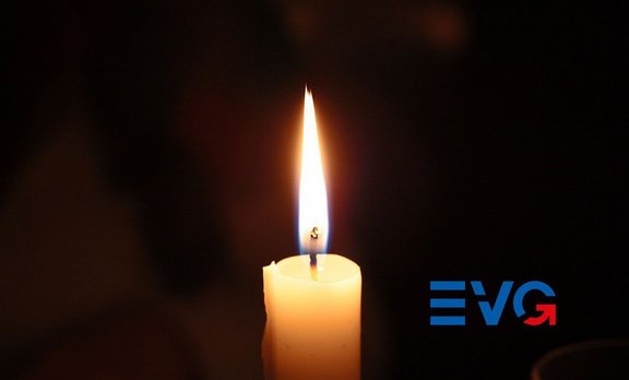 Brennende weiße Kerze im Vordergrund vor dunklem, unscharfem Hintergrund; rechts unten ein blau-rotes „EVG“-Logo.