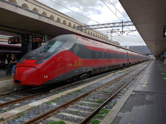 Ein roter Hochgeschwindigkeitszug mit der Aufschrift "italo" steht an einem überdachten Bahnsteig. 